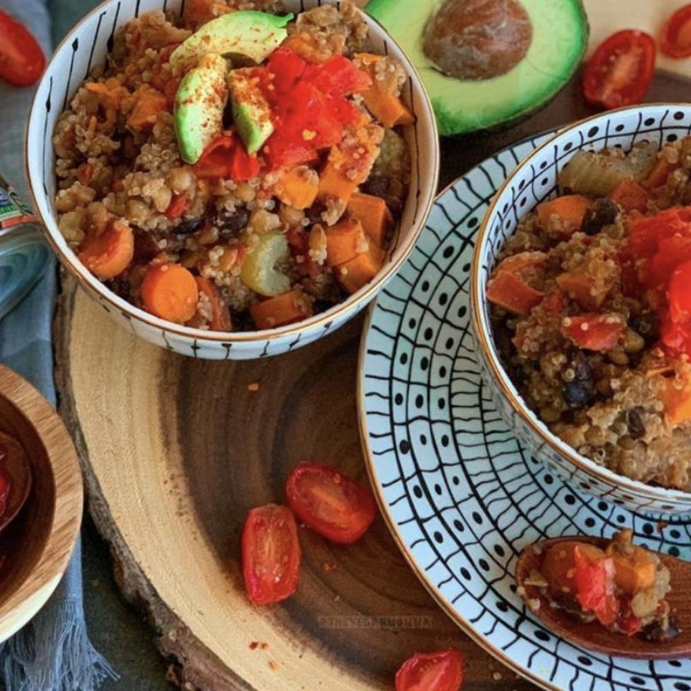 Two bowls of a quinoa dish with vegetables on a wooden board.