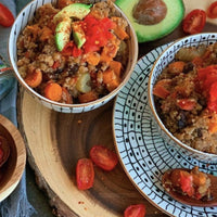 Two bowls of a quinoa dish with vegetables on a wooden board.