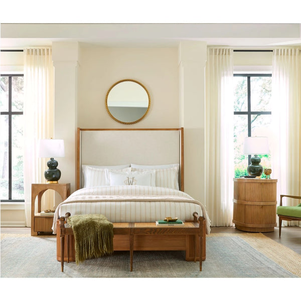 A mid-century modern wooden bed frame with a tall upholstered headboard, styled in a bright, neutral-toned bedroom with cream curtains, a wooden bench, and matching nightstands.