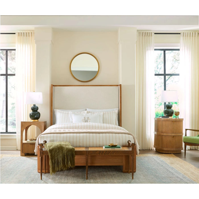 A mid-century modern wooden bed frame with a tall upholstered headboard, styled in a bright, neutral-toned bedroom with cream curtains, a wooden bench, and matching nightstands.