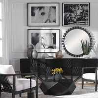 A contemporary living room showcasing black and white horse photos as the centerpiece, enhanced by a distressed black geometric table, the Cyra Burst Black Mirror by Uttermost, and stylish furniture.