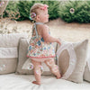 A baby in a floral dress stands on a couch surrounded by bubbles, creating a vintage vibe with Sugarboo & Co.'s stonewashed pillow.