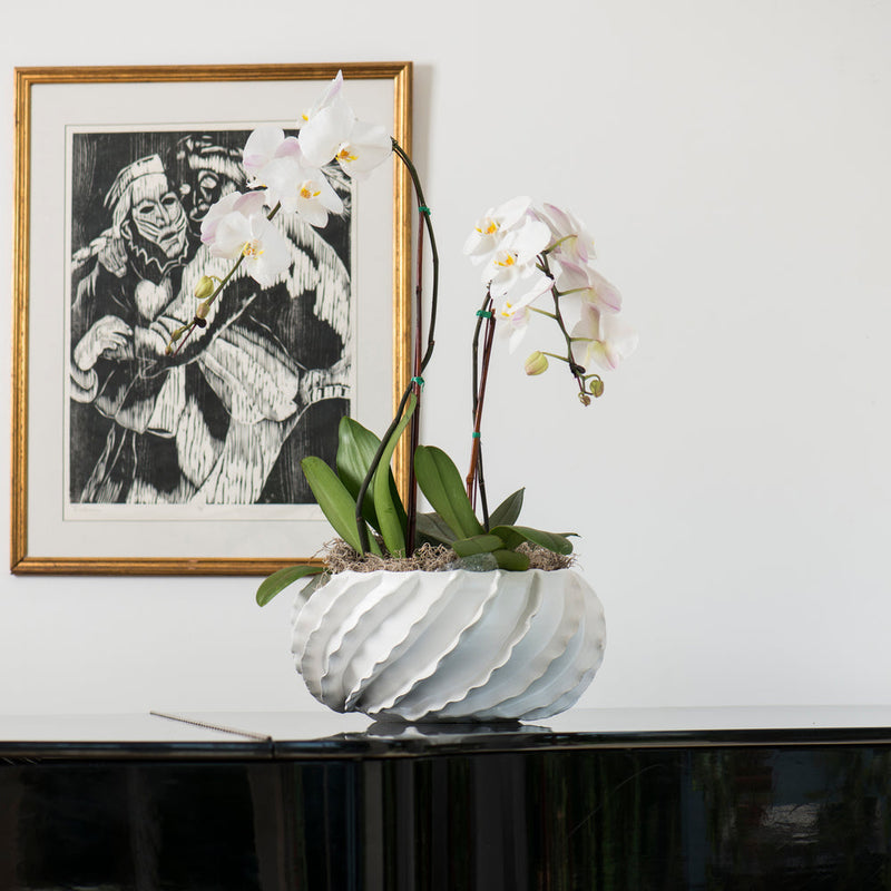 White orchids in a wavy pot grace the piano, accompanied by framed artwork and the Santa Barbara Decorative Bowl Matte White by Abigails, adorned with ceramic ribbons, in the background.