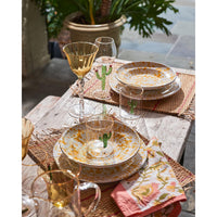 An outdoor table set featuring patterned dishes is beautifully enhanced by the Abigails Aztec Cactus Tumblers + Pitcher Set, complete with floral napkins stylishly placed on woven placemats.