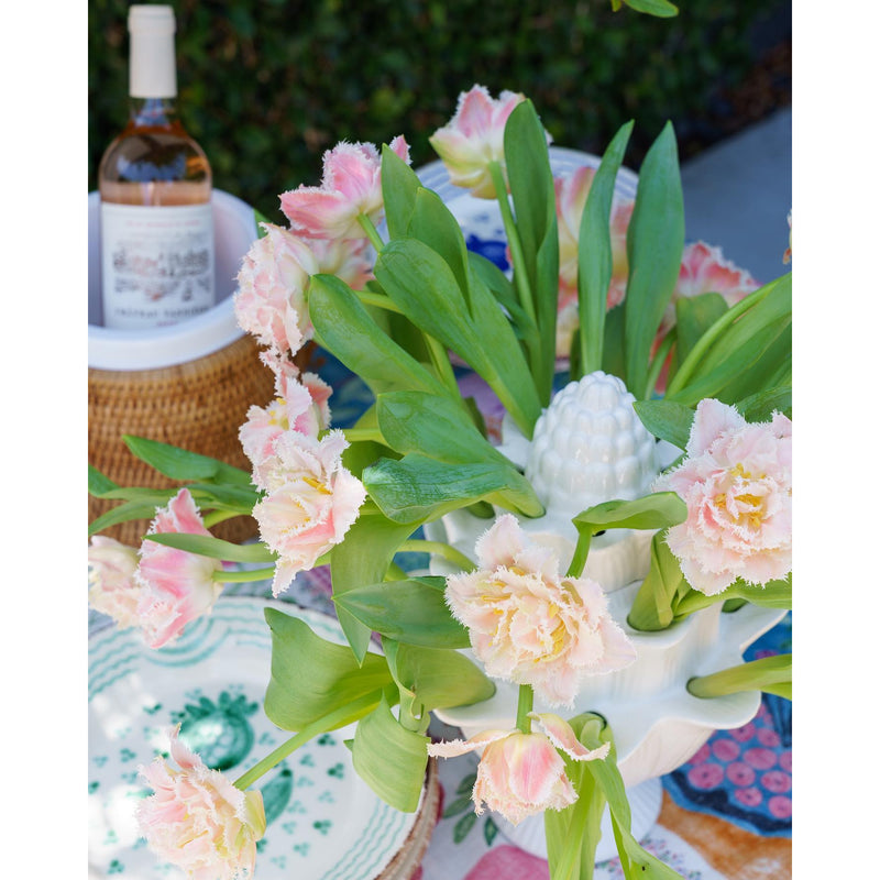 A bouquet of pink frilled tulips arranged in an Abigails Small Ivory Artichoke Tulipiere graces the table, enhancing the elegant dining room display with a bottle of wine subtly nestled in the background.