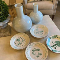 Two white vases and six Abigails Casa Nuno Green Pomegranate Dinner Plates adorn the living room table.