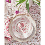 A floral-patterned table setting featuring a decorative plate, a 100% cotton tablecloth, Abigails' Pomegranate Cabana Napkins (set of 4) made of block printed cotton, and tulips in a vase.