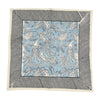 Set of 4 square napkins named Flowers + Feathers Cabana from Abigails, featuring a blue and white birds and flowers pattern, bordered by black and white diagonal stripes.