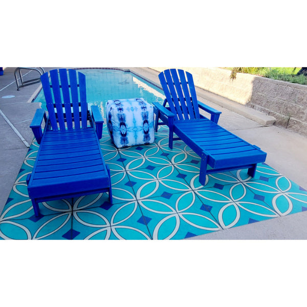 Two blue lounge chairs by a pool, one with a tie-dye towel, on Pattern 70 Echoes From The Bells Vinyl Floorcloth.