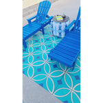 Two blue Adirondack chairs on a Pattern 70 Echoes From The Bells vinyl floorcloth by a small table with books and a candle.