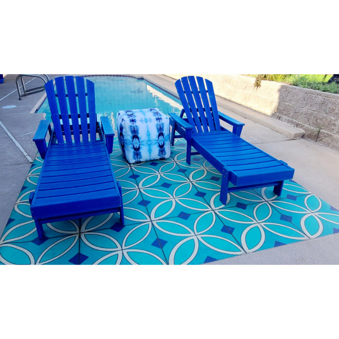 Two blue lounge chairs by a pool, one with a tie-dye towel, on Pattern 70 Echoes From The Bells Vinyl Floorcloth.