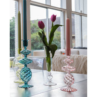 Colorful **Pink Swirl Glass Candlesticks** by Abigails and a transparent glass vase with pink tulips sit on a table in front of large windows with a backyard view.