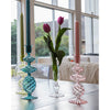 Colorful **Pink Swirl Glass Candlesticks** by Abigails and a transparent glass vase with pink tulips sit on a table in front of large windows with a backyard view.