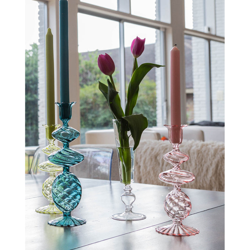 Colorful **Pink Swirl Glass Candlesticks** by Abigails and a transparent glass vase with pink tulips sit on a table in front of large windows with a backyard view.