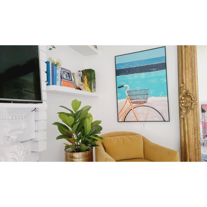 Living room with a yellow chair, potted plant, Kalalou's Oil Painting Bicycle Wall Art framed on the wall, and shelves with books and decor in a coastal home.
