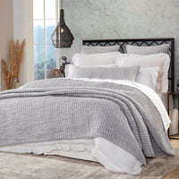 A neatly made bed with the Bella Gray Bedding Collection by Orchids Lux Home and white pillows, in a cozy bedroom with a window and plants.