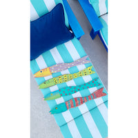Hand-painted, vibrant fish sculptures crafted from reclaimed distressed wood by Kalalou rest on a striped blue and white lounge chair, accompanied by a cushion and another chair. These colorful Painted Recycled Wood Wall Art pieces (set of 4) bring joy to the serene setting.