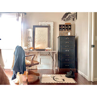 Transform your home office into a charming vintage-inspired space with a wooden desk and tall drawers alongside a comfortable chair draped with a jacket. Enhance the warmth and appeal of the room with the rustic charm of Sugarboo & Co.'s Book Collection Maya Angelou Wall Art, available in various size and color options.