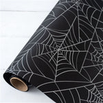 The Halloween Spiderweb Paper Table Runner by Hester & Cook unfurled on a white surface, making it the perfect addition for creating a spooky tablescape at your next Halloween party.