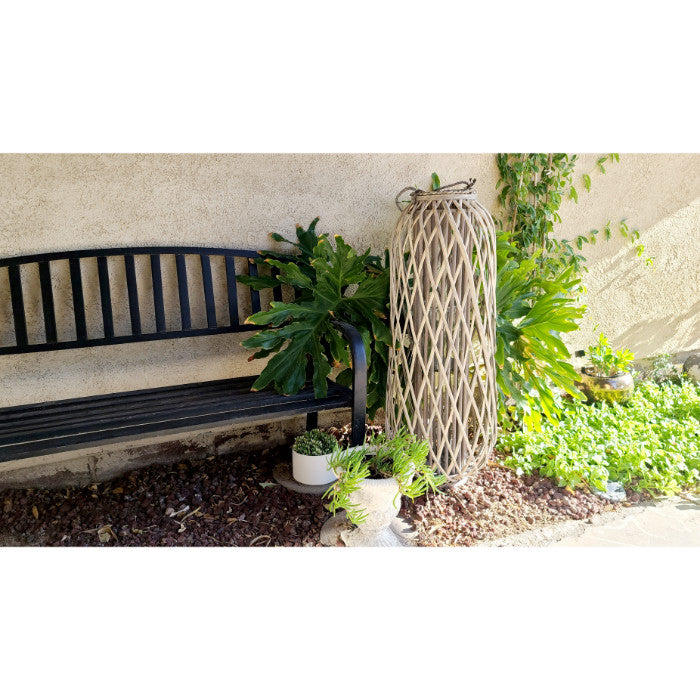 Black bench, potted plants, and the Kalalou Willow Extra Large Glass Candle Lantern featuring a driftwood tone against a beige wall adorned with vines.
