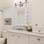 Bathroom with Uttermost Resin Sea Coral Wall Mirror, marble countertop, white cabinets, floral decor, and framed flower artwork.