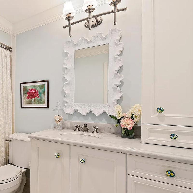 Bathroom with Uttermost Resin Sea Coral Wall Mirror, marble countertop, white cabinets, floral decor, and framed flower artwork.