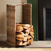 Near the fireplace, a Napa Home & Garden Rattan Log Basket - Tall sits on the wooden floor, filled with firewood.