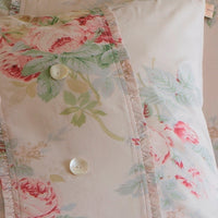 Close-up of a 100% cotton pillowcase from the Shore Rose Petal Bedding Collection by Taylor Linens, adorned with large white buttons and a floral pattern featuring pink and green flowers. This shabby chic design adds a charming touch to any bedroom decor.