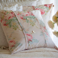 Floral pillows featuring pink and green patterns with button accents beautifully complement the white textured bedspread, all part of Taylor Linens' Shore Rose Petal Bedding Collection.