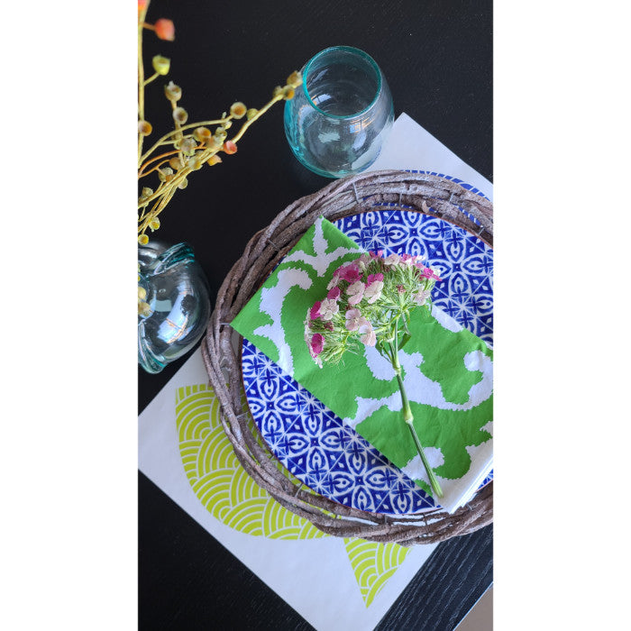 A holiday tablescape showcasing a blue patterned plate, green napkin, and a small bouquet graces the surface of a Kalalou Rustic Grey Twig Charger alongside an elegant glass.