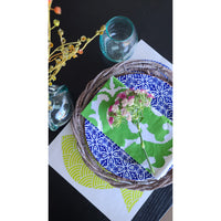 A holiday tablescape showcasing a blue patterned plate, green napkin, and a small bouquet graces the surface of a Kalalou Rustic Grey Twig Charger alongside an elegant glass.