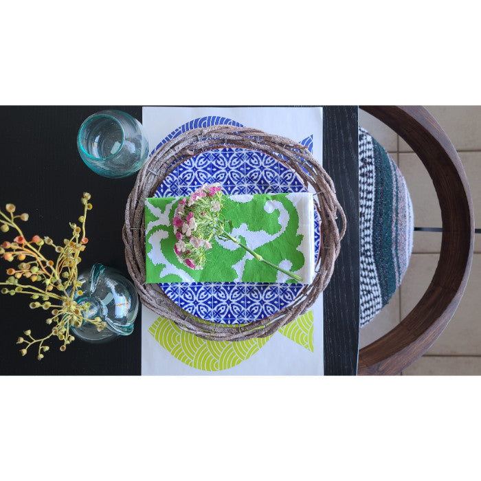 Top view of a holiday tablescape featuring a wreath, a green and white card, elegant plates on Kalalou's Rustic Grey Twig Charger set, a vase with berries, and two glasses.