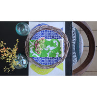 Top view of a holiday tablescape featuring a wreath, a green and white card, elegant plates on Kalalou's Rustic Grey Twig Charger set, a vase with berries, and two glasses.