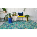 Geometric rug and potted plants, yellow bench with an Outdoor Newbury Velvet Indigo Lumbar pillow, and bar cart in chic room.