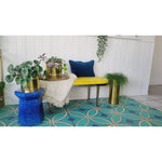 Colorful seating, blue table, potted plants, yellow bench, and a vinyl floorcloth from Spicher and Co ('Pattern 70 Echoes').