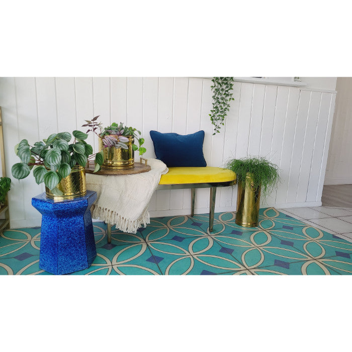 Colorful seating, blue table, potted plants, yellow bench, and a vinyl floorcloth from Spicher and Co ('Pattern 70 Echoes').