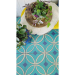 Plants in woven baskets on a yellow table atop Spicher and Company vinyl floorcloth featuring teal circular patterns.