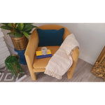 Indigo lumbar by Lacefield Designs on yellow chair with white blanket, books, mug, potted plants & decorative frame nearby.
