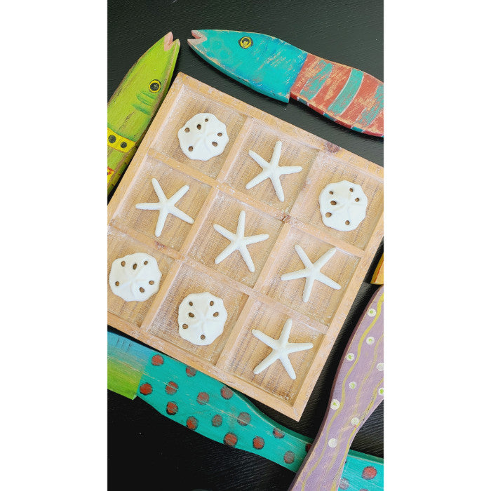 The Painted Recycled Wood Wall Art (set of 4) by Kalalou features a tic-tac-toe board with starfish and sand dollars as pieces, surrounded by colorful wooden fish on a black background, all hand-painted in vibrant tropical colors.
