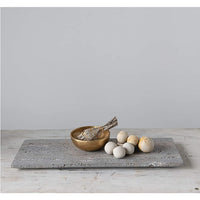The Travertine Marble Serving Tray by BSEID, featuring a wooden bowl, a bundle of herbs, and round white stones, creates an organic aesthetic on the minimalist surface. The natural vibe is further enhanced by the travertine marble finish, seamlessly blending into any serene space.